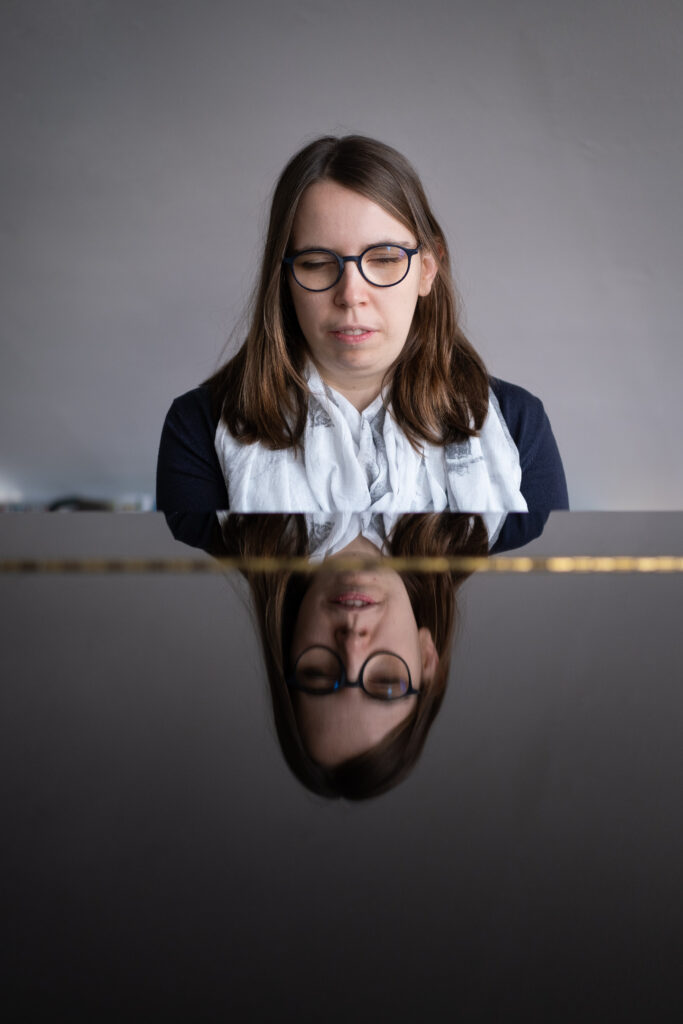 Lorena Dürnholz spielt mit geschlossenen Augen Klavier, ihr Gesicht spiegelt sich im schwarzen Klavierlack