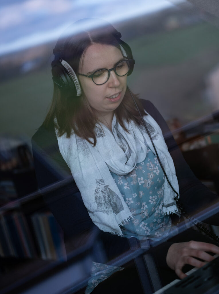 Blick durch ein Fenster: Lorena Dürnholz trägt einen Kopfhörer und spielt auf dem Stagepiano