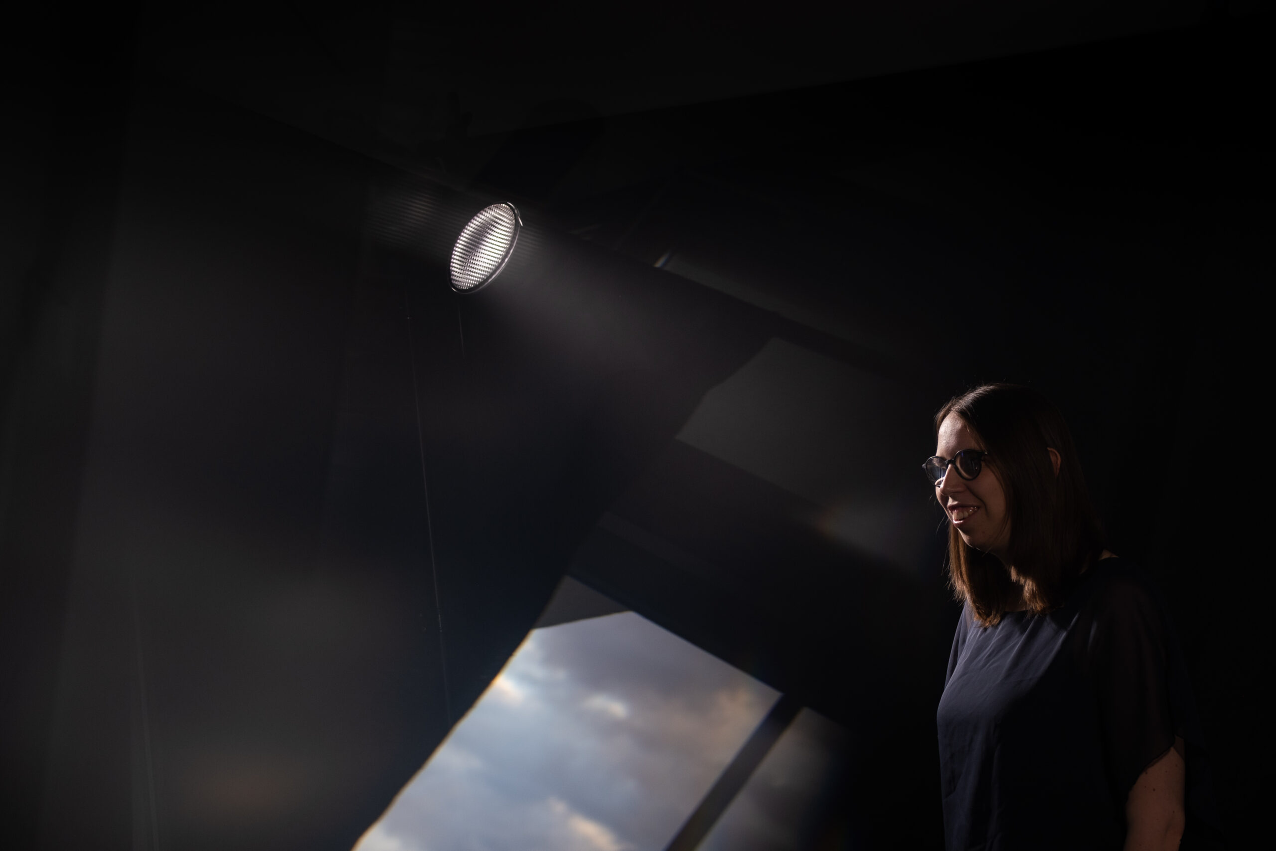 Lorena Dürnholz steht im Lichtkegel eines Bühnenscheinwerfers und lächelt – im Vordergrund sind Spiegelungen eines Wolkenhimmels zu erkennen