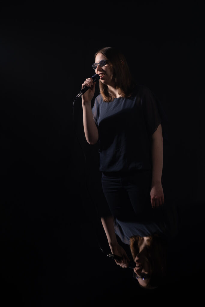 Lorena Dürnholz steht mit einem Mikrofon in der Hand hinter einem Konzertflügel und singt