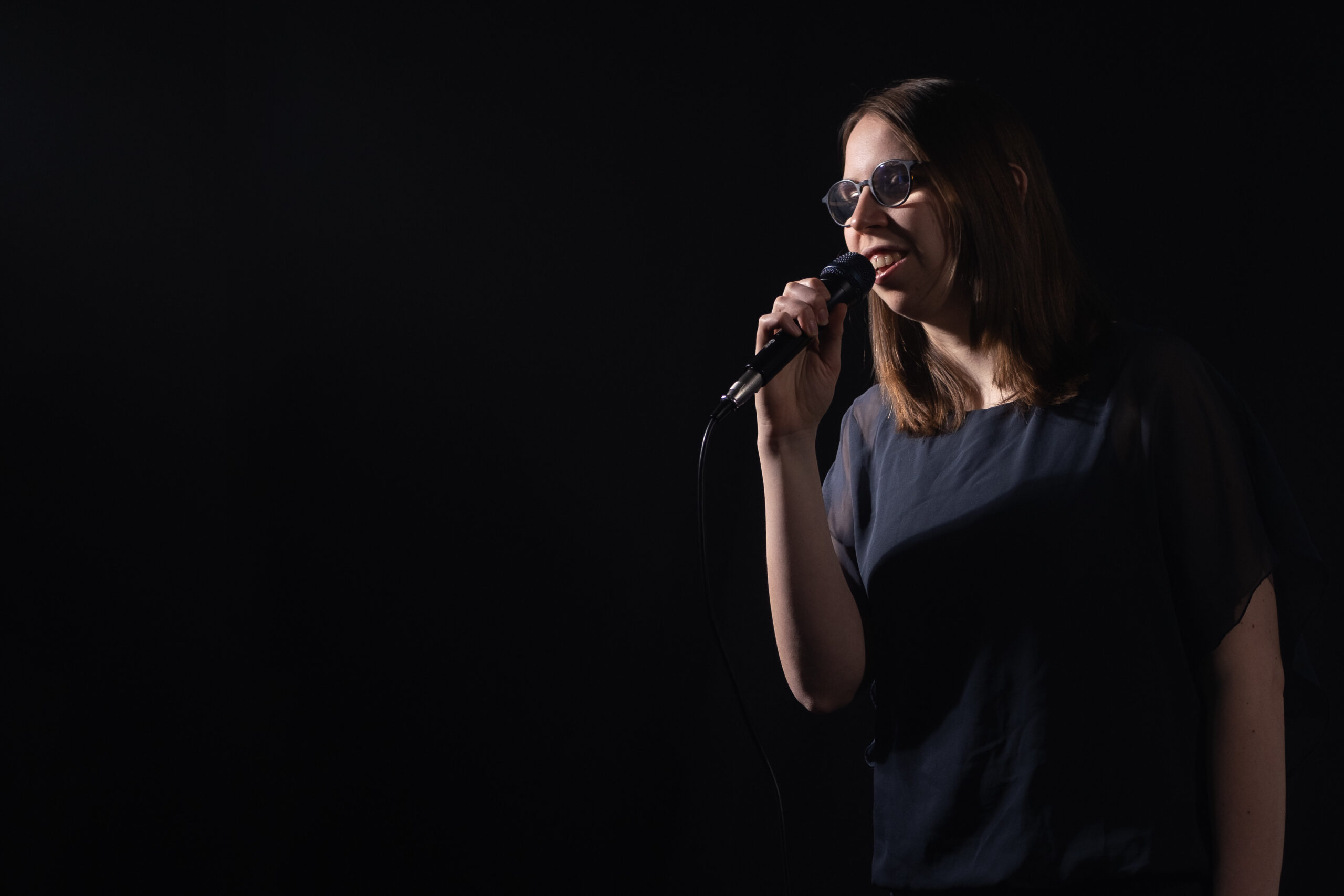 Lorena Dürnholz steht mit einem Mikrofon vor dunklem Hintergrund im Scheinwerferlicht und singt
