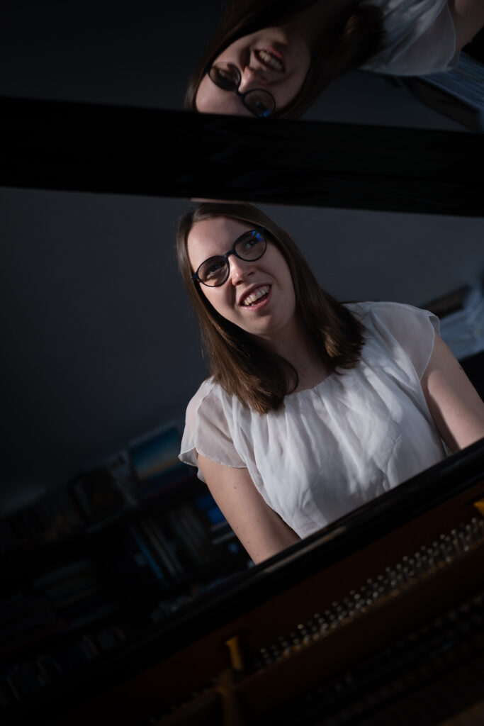 Lorena Dürnholz sitzt lächelnd an einem Konzertflügel – im geöffneten Deckel des Instruments spiegelt sich ihr Gesicht