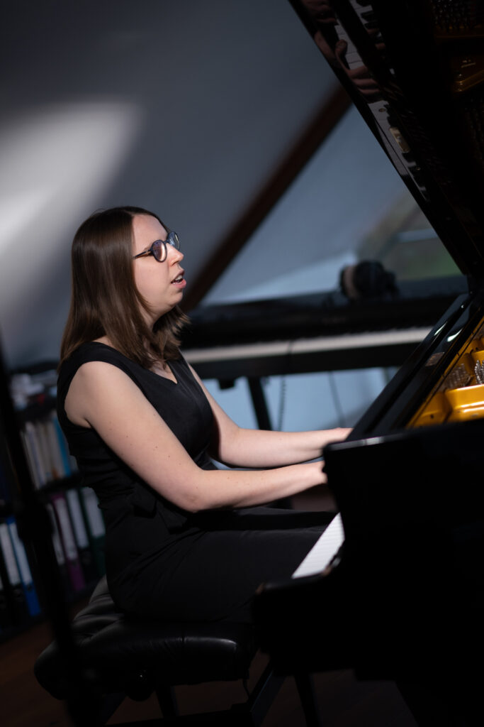 Lorena Dürnholz spielt auf einem geöffneten Konzertflügel, im Hintergrund sind (unscharf gestellt) ein Stagepiano und Bücherregale zu erkennen